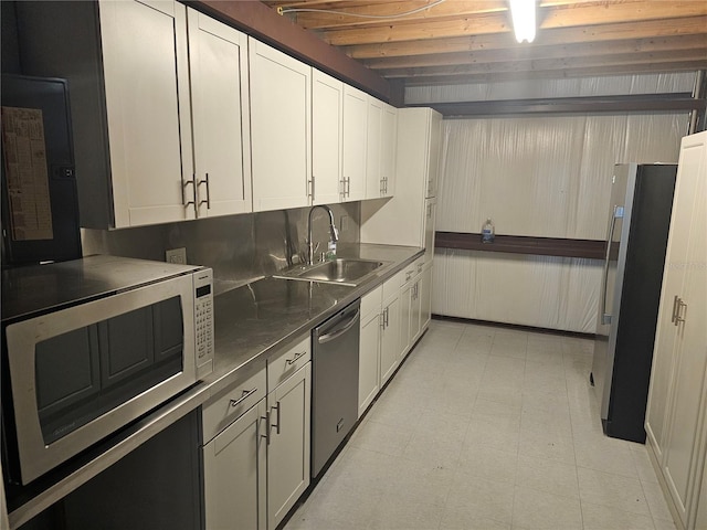 kitchen with white cabinetry, sink, stainless steel counters, stainless steel appliances, and beamed ceiling