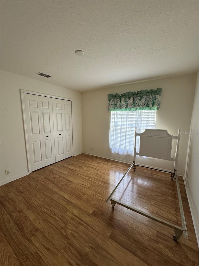 unfurnished bedroom featuring hardwood / wood-style floors, a textured ceiling, and a closet