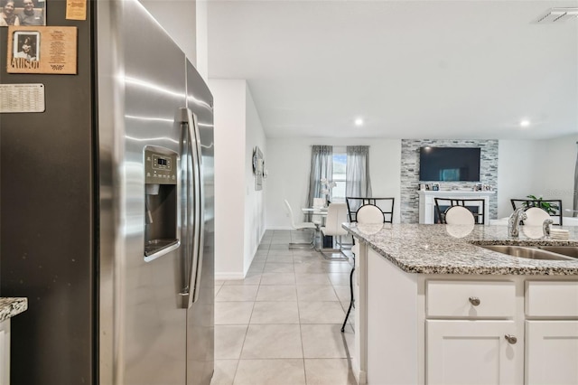 kitchen featuring white cabinets, stainless steel fridge, light stone countertops, and sink