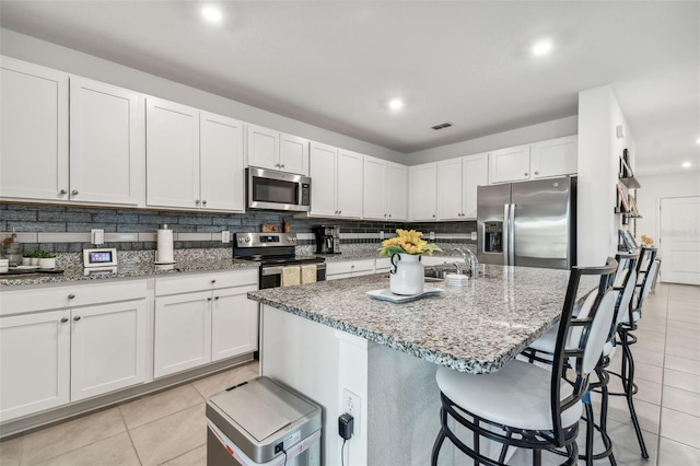 kitchen with white cabinets, stainless steel appliances, a kitchen island with sink, and a breakfast bar area