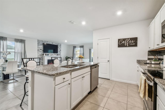 kitchen with light stone countertops, appliances with stainless steel finishes, sink, a center island with sink, and white cabinets