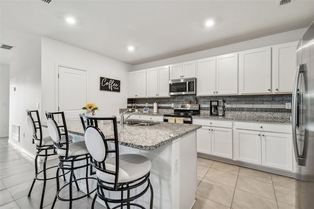 kitchen with white cabinetry, sink, light stone counters, a center island with sink, and appliances with stainless steel finishes