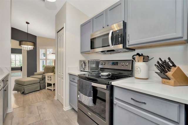 kitchen featuring light hardwood / wood-style flooring, a chandelier, decorative light fixtures, lofted ceiling, and appliances with stainless steel finishes