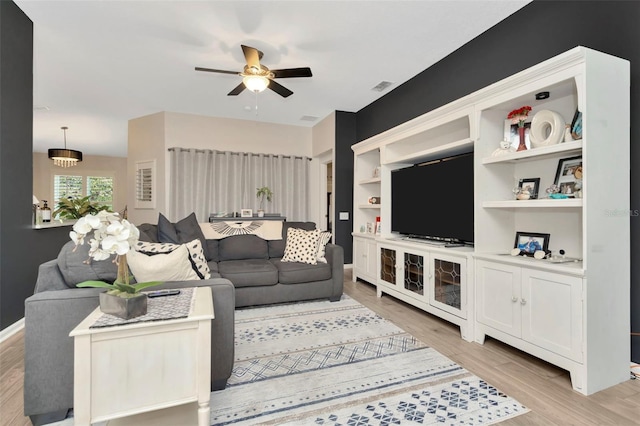 living room with built in shelves, ceiling fan, and light wood-type flooring