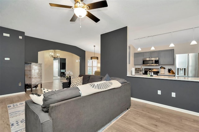 living room featuring lofted ceiling, rail lighting, ceiling fan with notable chandelier, and light wood-type flooring