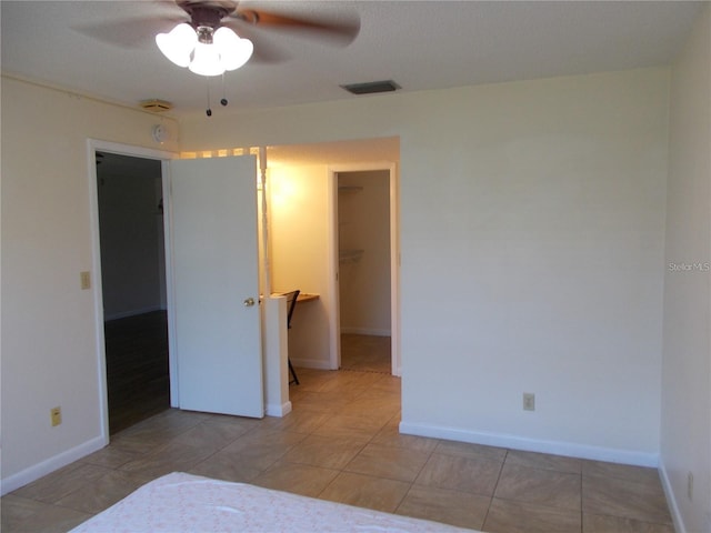 unfurnished bedroom with light tile patterned floors, a walk in closet, a closet, and ceiling fan