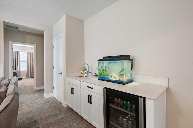 bar with white cabinets, sink, wine cooler, carpet flooring, and a textured ceiling