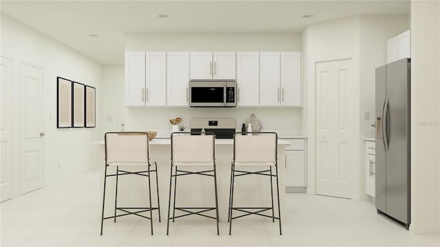 kitchen featuring light tile patterned floors, a kitchen breakfast bar, a center island with sink, white cabinets, and appliances with stainless steel finishes