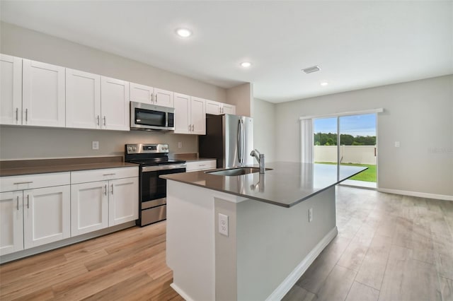 kitchen featuring appliances with stainless steel finishes, sink, white cabinets, light hardwood / wood-style floors, and an island with sink