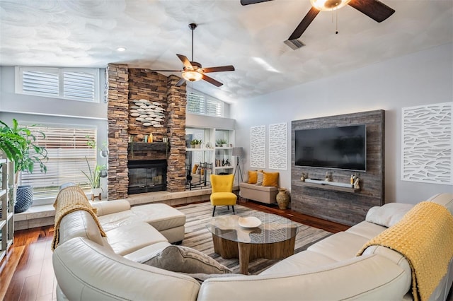 living room featuring hardwood / wood-style floors, ceiling fan, a stone fireplace, and lofted ceiling