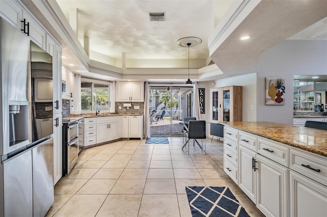 kitchen featuring appliances with stainless steel finishes, a tray ceiling, decorative light fixtures, light stone counters, and white cabinetry