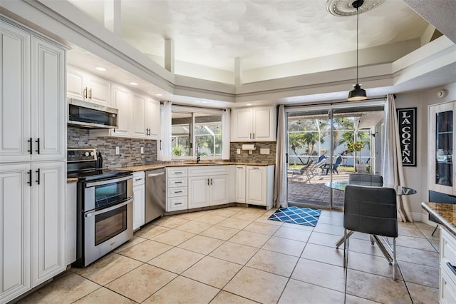 kitchen with white cabinets, light tile patterned floors, appliances with stainless steel finishes, a tray ceiling, and decorative light fixtures