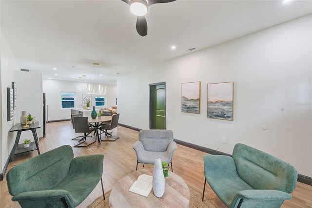 living room featuring ceiling fan with notable chandelier and light hardwood / wood-style floors