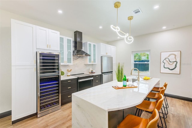 kitchen featuring stainless steel appliances, beverage cooler, wall chimney range hood, and an island with sink