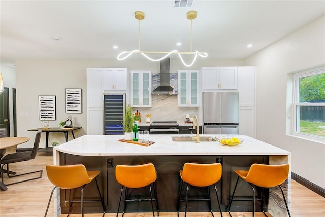 kitchen with wall chimney exhaust hood, a center island with sink, tasteful backsplash, appliances with stainless steel finishes, and sink