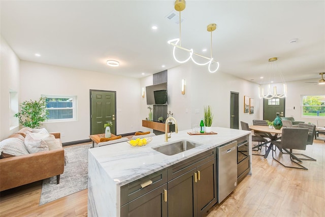 kitchen featuring a kitchen island with sink, pendant lighting, light stone counters, sink, and stainless steel dishwasher