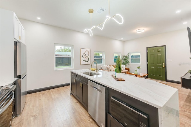 kitchen featuring a center island with sink, stainless steel appliances, pendant lighting, light stone counters, and sink