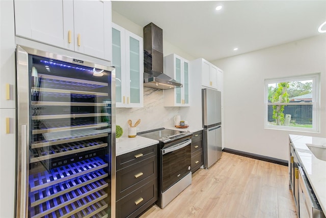 kitchen featuring light stone counters, wall chimney range hood, beverage cooler, white cabinetry, and appliances with stainless steel finishes