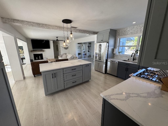 kitchen featuring gray cabinets, a large fireplace, sink, light stone counters, and stainless steel appliances