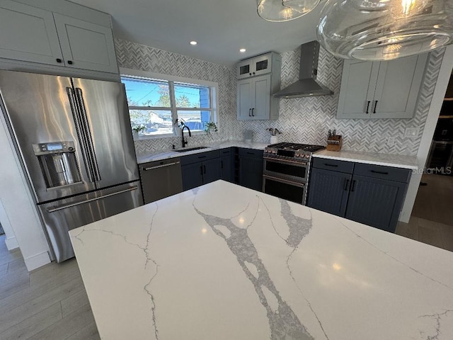 kitchen with wall chimney range hood, sink, gray cabinets, stainless steel appliances, and light stone counters