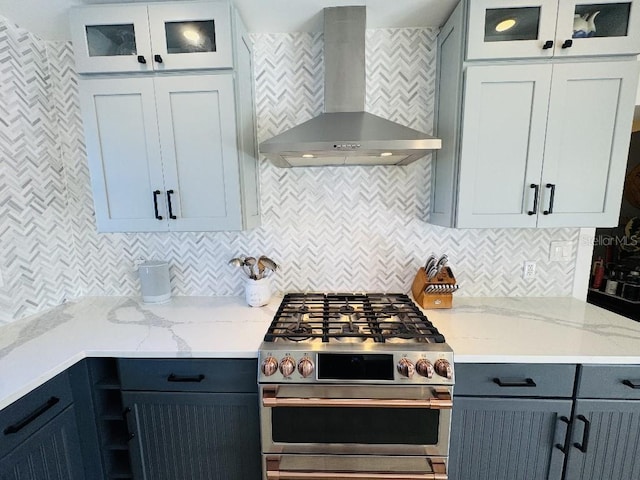 kitchen with tasteful backsplash, wall chimney exhaust hood, stainless steel gas range, and light stone counters