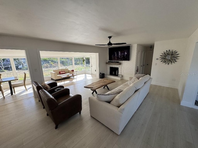 living room featuring a fireplace, ceiling fan, and light wood-type flooring