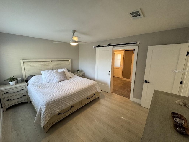 bedroom featuring ceiling fan, a barn door, and light hardwood / wood-style floors