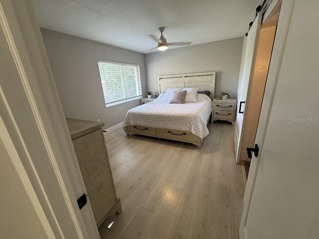 bedroom featuring ceiling fan, a barn door, and light wood-type flooring