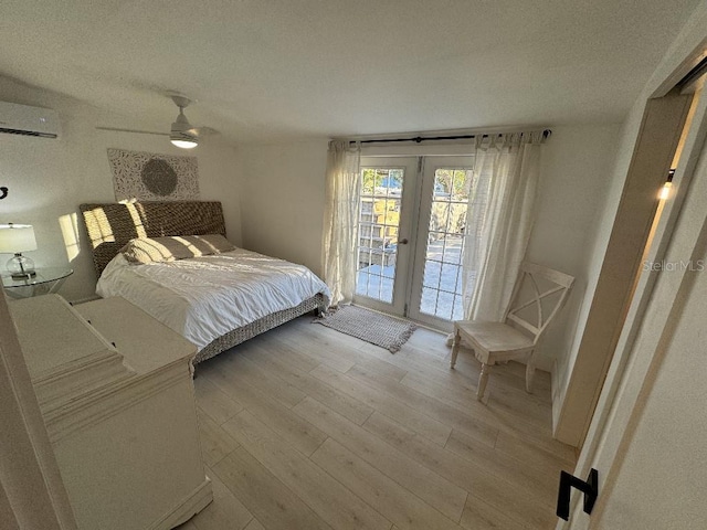 bedroom featuring french doors, light wood-type flooring, access to outside, a wall unit AC, and ceiling fan