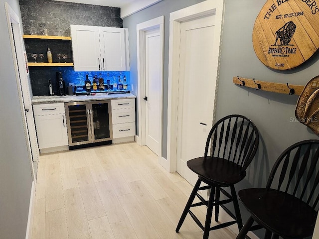 bar featuring decorative backsplash, beverage cooler, white cabinets, and light wood-type flooring