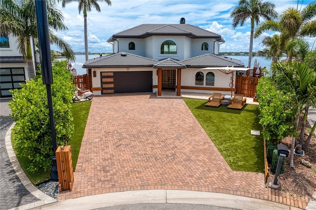 mediterranean / spanish home with a garage, a water view, and a front lawn