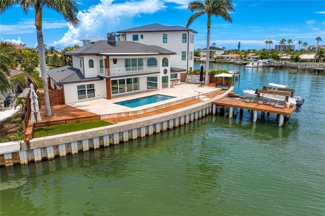 back of house with a swimming pool with hot tub, a balcony, a patio, and a water view