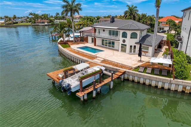 back of property featuring a patio area, a balcony, a water view, and a pool with hot tub