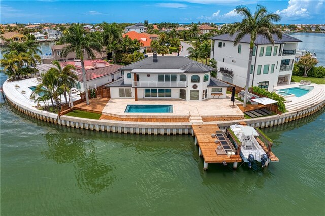 back of house with a water view, a swimming pool with hot tub, a balcony, and a patio