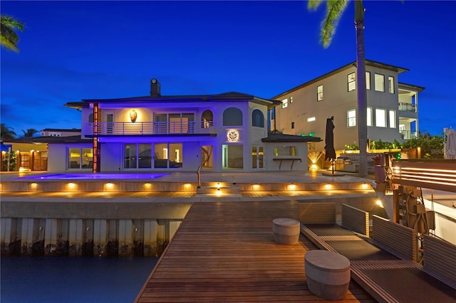 back house at night with a balcony and a pool side deck