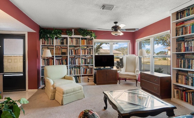 living area with ceiling fan, a textured ceiling, and light carpet