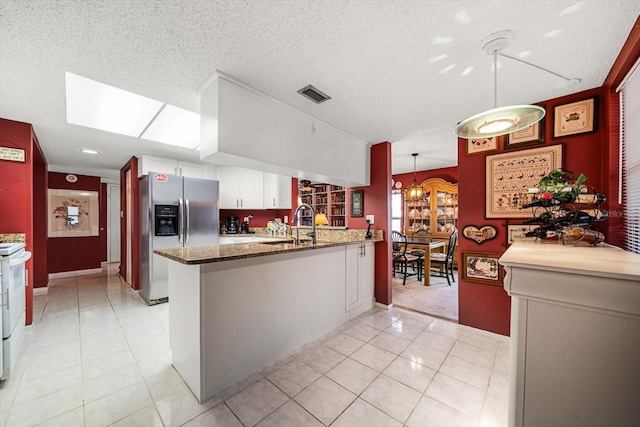 kitchen with kitchen peninsula, stainless steel fridge, decorative light fixtures, and white cabinetry