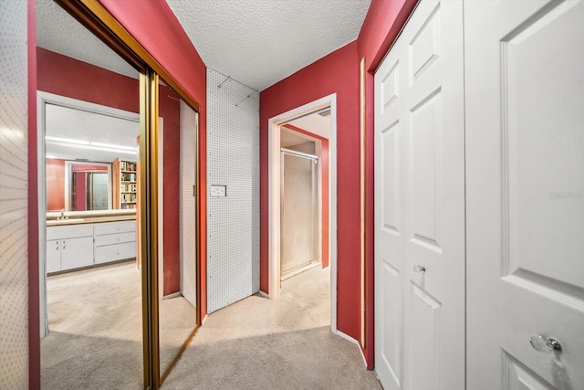 hallway with a textured ceiling, light colored carpet, and sink