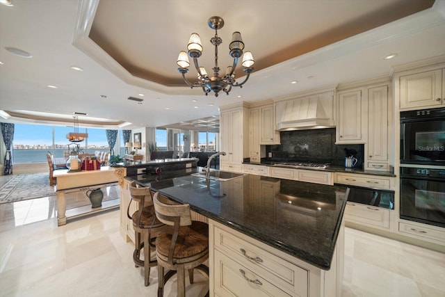 kitchen with sink, cream cabinets, decorative light fixtures, a water view, and custom range hood