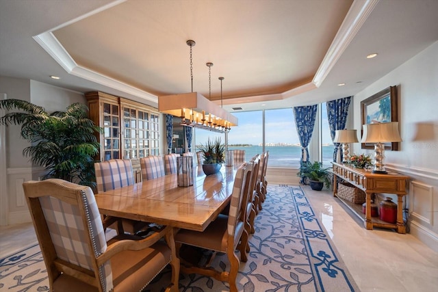 dining area with a chandelier, ornamental molding, a water view, and a tray ceiling