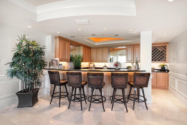 kitchen featuring a raised ceiling, crown molding, light brown cabinetry, kitchen peninsula, and a breakfast bar area