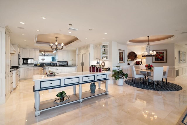 kitchen with a raised ceiling, open shelves, an island with sink, and an inviting chandelier