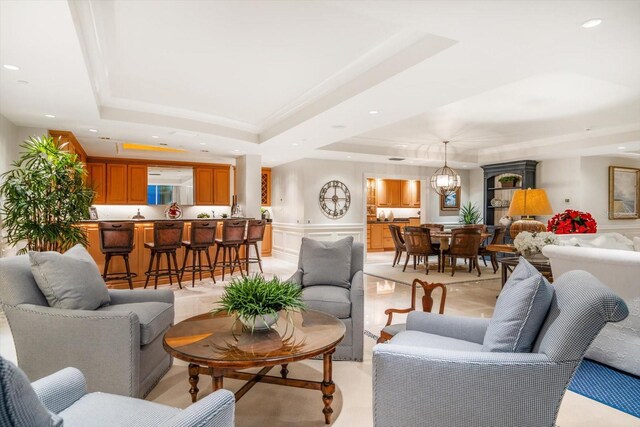 living room with a raised ceiling, a wainscoted wall, crown molding, a chandelier, and recessed lighting