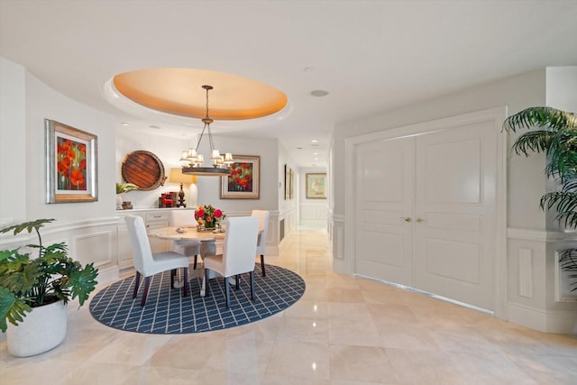 dining room featuring an inviting chandelier, a tray ceiling, a decorative wall, and wainscoting