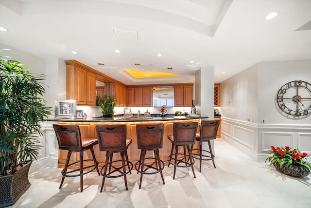 kitchen with a tray ceiling, recessed lighting, visible vents, a decorative wall, and wainscoting