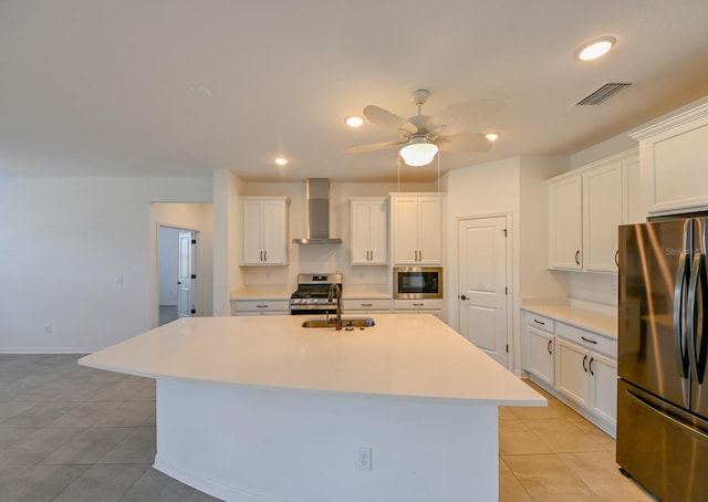 kitchen featuring appliances with stainless steel finishes, wall chimney exhaust hood, ceiling fan, white cabinets, and an island with sink