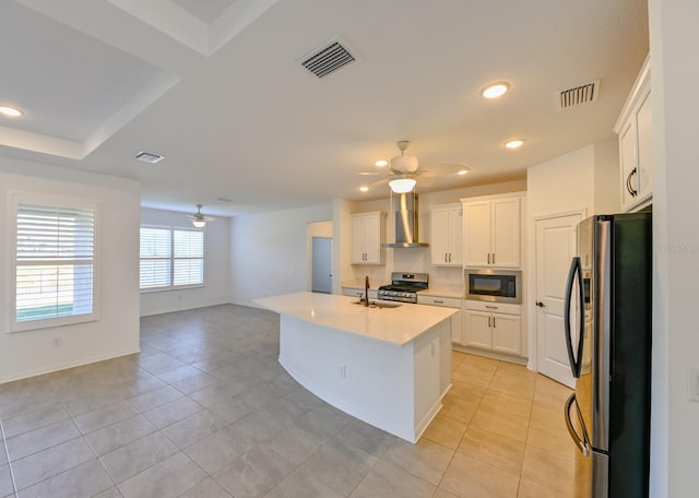 kitchen featuring sink, wall chimney exhaust hood, stainless steel appliances, a kitchen island with sink, and white cabinets