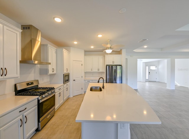 kitchen with appliances with stainless steel finishes, a kitchen island with sink, sink, wall chimney range hood, and white cabinets