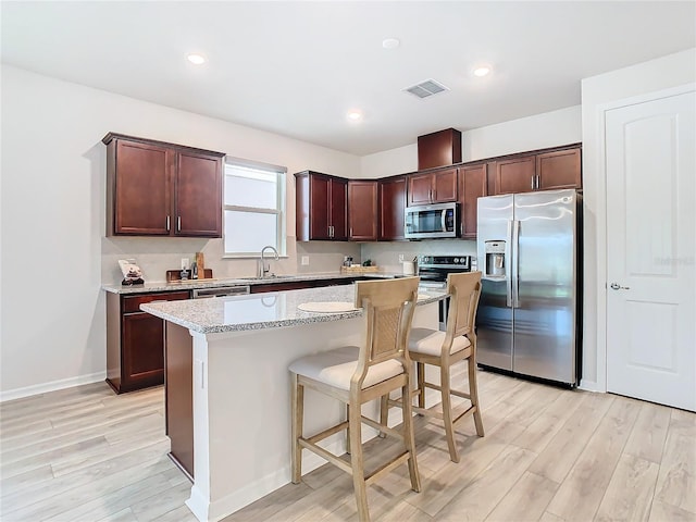 kitchen featuring stainless steel appliances, light stone counters, a breakfast bar, a kitchen island, and light wood-type flooring