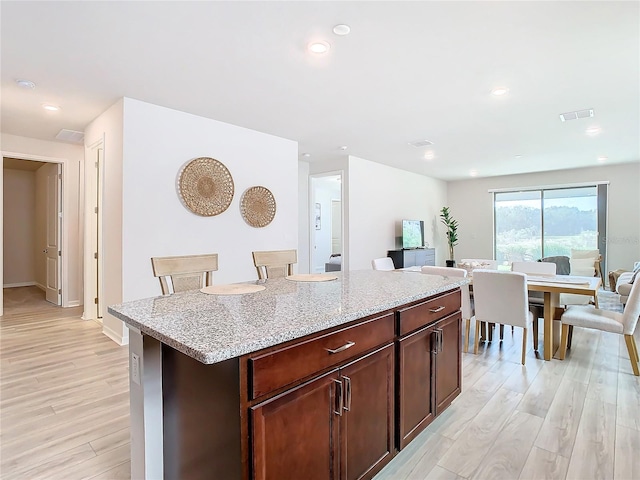 kitchen with a center island, a kitchen bar, light hardwood / wood-style flooring, light stone counters, and dark brown cabinetry